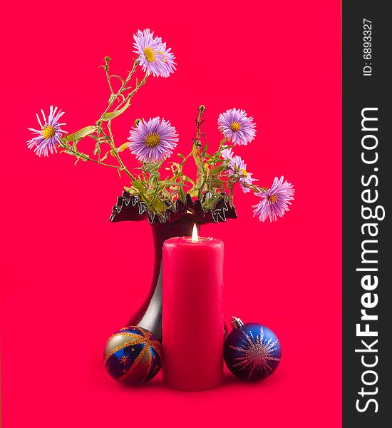 Red burning candle with New Year's spheres and bouquet blue colors in black vase on red background. Red burning candle with New Year's spheres and bouquet blue colors in black vase on red background