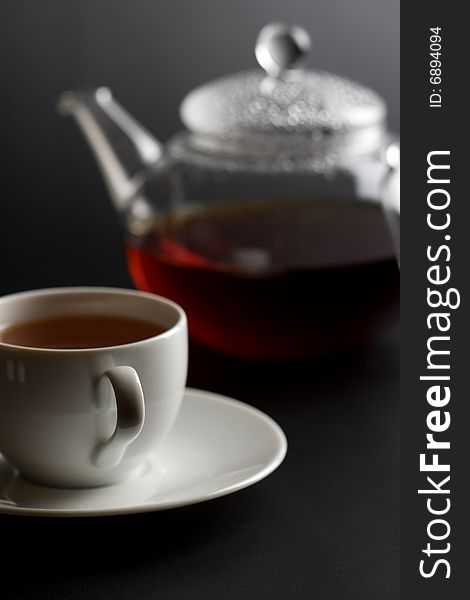 Cup of tea and tea pot over dark background
