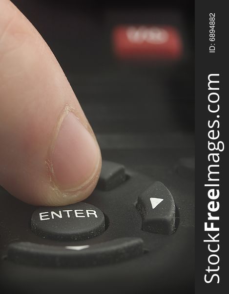 Man finger pushing ENTER on a black remote control