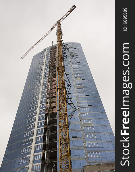 A blue high rise tower with yellow crane against sky. A blue high rise tower with yellow crane against sky