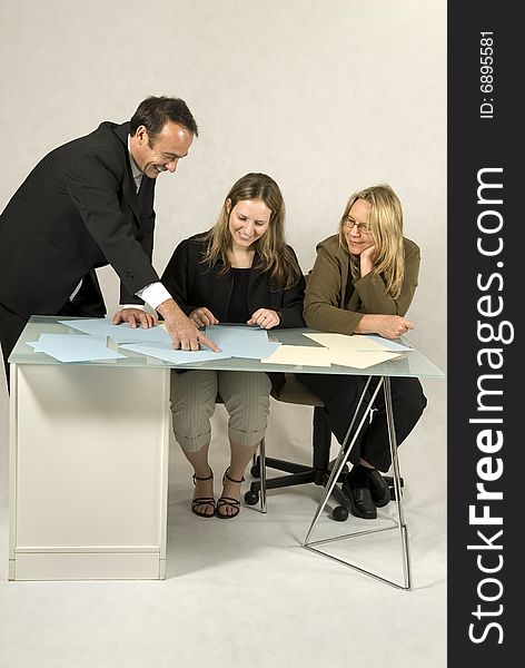 Three people are in a business meeting. They are smiling and looking at pieces of paper in front of them. Vertically framed shot. Three people are in a business meeting. They are smiling and looking at pieces of paper in front of them. Vertically framed shot.