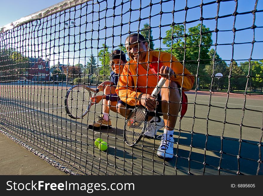 Male and female tennis players crouching behind the net smiling.. They are holding rackets and two tennis balls are in front of them. Vertically framed photo. Male and female tennis players crouching behind the net smiling.. They are holding rackets and two tennis balls are in front of them. Vertically framed photo.