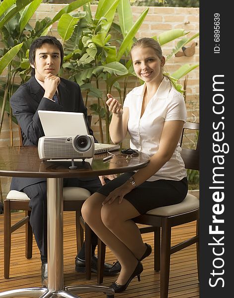 Man and woman with a projector and a laptop.. They are seated and she is smiling while he looks pensive. Vertically framed photo. Man and woman with a projector and a laptop.. They are seated and she is smiling while he looks pensive. Vertically framed photo.