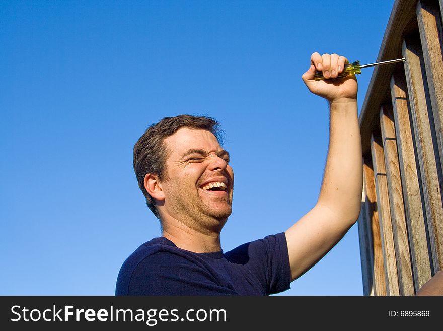 Laughing man using screwdriver to fix porch. Horizontally framed photo. Laughing man using screwdriver to fix porch. Horizontally framed photo.