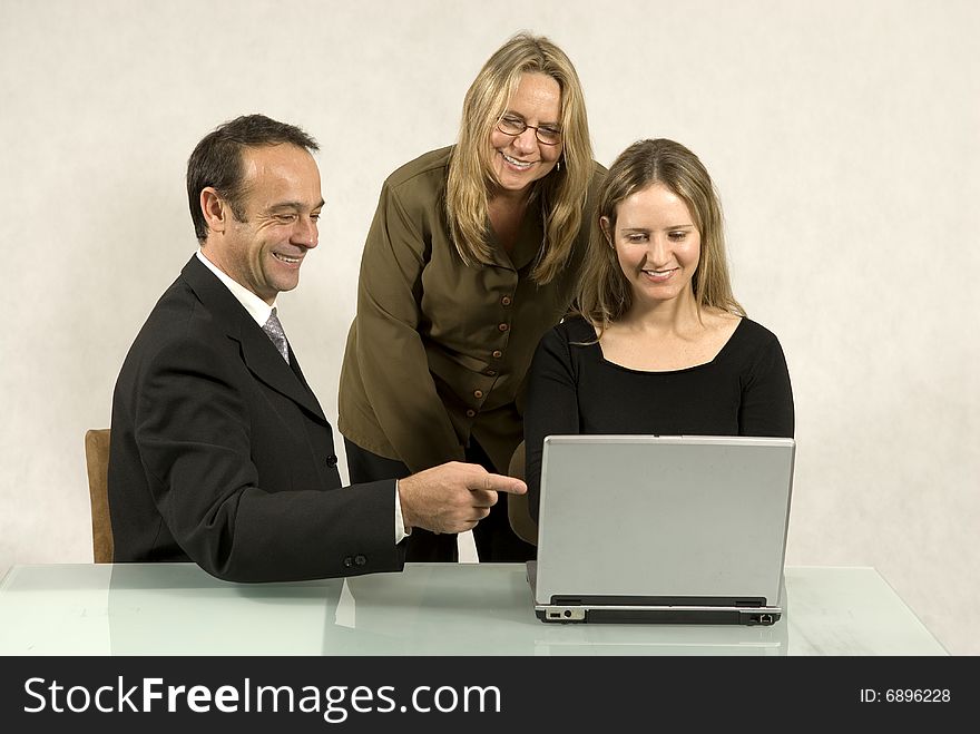 Three people are in a business meeting. They are smiling and looking at the screen of the laptop. Horizontally framed shot. Three people are in a business meeting. They are smiling and looking at the screen of the laptop. Horizontally framed shot.