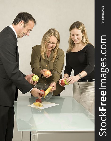 Three people are in an office.  It appears that they are about to arrange the fruit into the glass bowl.  Vertically framed shot. Three people are in an office.  It appears that they are about to arrange the fruit into the glass bowl.  Vertically framed shot.