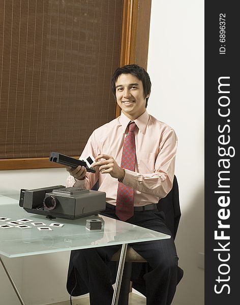 Man smiling as he looks at a slide next to a projector. Vertically framed photo. Man smiling as he looks at a slide next to a projector. Vertically framed photo.