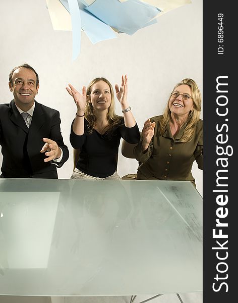 Three people are in an office in a meeting.  They are smiling and throwing papers in the air in success.  Vertically framed shot. Three people are in an office in a meeting.  They are smiling and throwing papers in the air in success.  Vertically framed shot.