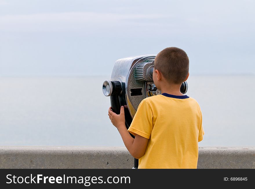The boy looks through the coin operated binoculars on horizon. The boy looks through the coin operated binoculars on horizon
