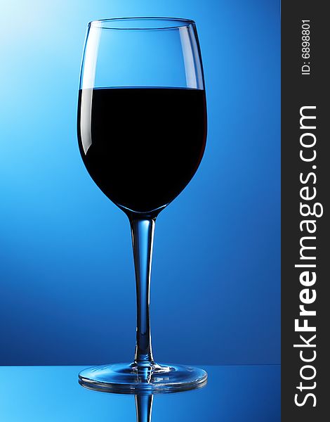 A glass of red wine on a reflective surface with blue graduated background. A glass of red wine on a reflective surface with blue graduated background.