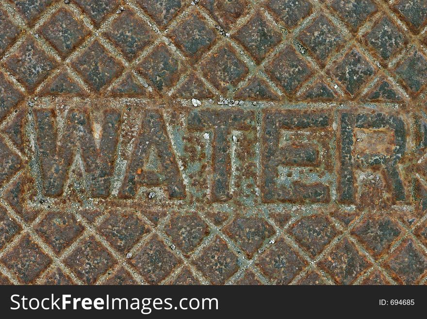 Iron cover over water turn-off valve has the word water inscribed upon it, along with decorative squares. Iron cover over water turn-off valve has the word water inscribed upon it, along with decorative squares