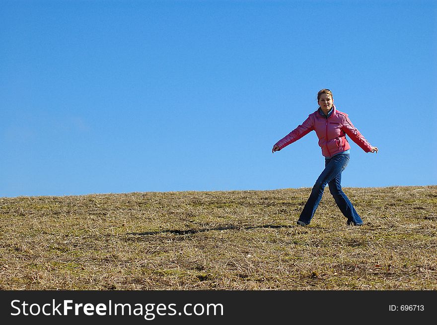 Young woman dressed magenta jacket and jeans playing around meadow with clean blue sky as background. Young woman dressed magenta jacket and jeans playing around meadow with clean blue sky as background
