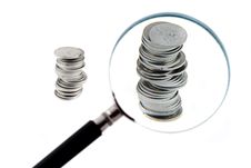 Magnifying Glass With Two Columns Of Coins Behind Royalty Free Stock Photos