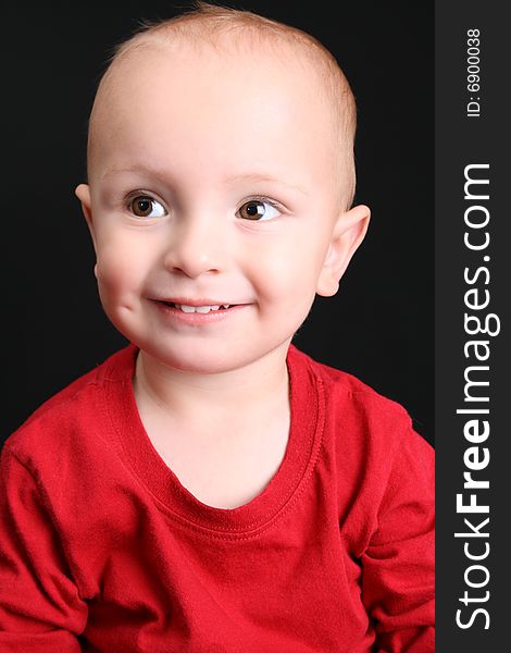 Blonde toddler against a black background with a big smile