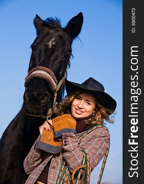 Lovely blond woman in a hat standing by horse in a field