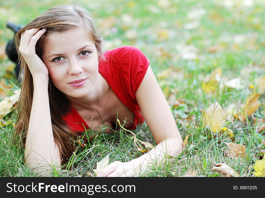 Young beautiful woman lying on the green grass with maple leaf. Young beautiful woman lying on the green grass with maple leaf