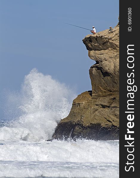 Fisherman on clifftop with dramatic waves crashing below.