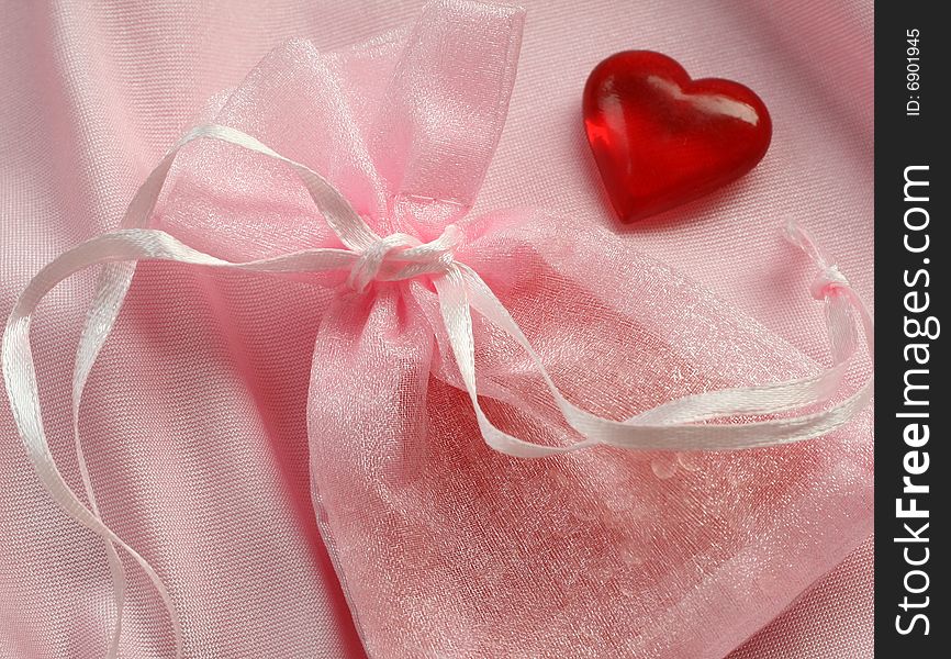 Small gift in rosy bag and red heart closeup