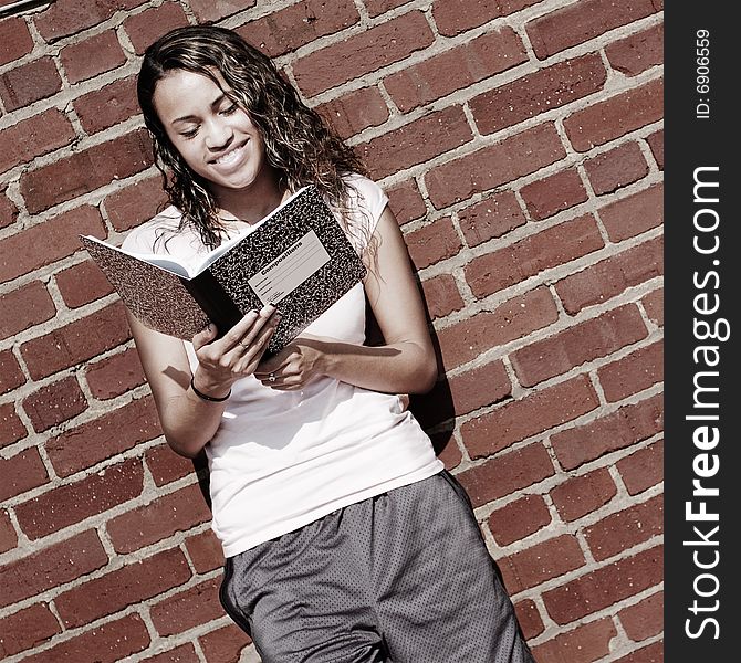 Beautiful young girl reading notebook against a brick wall. Beautiful young girl reading notebook against a brick wall.