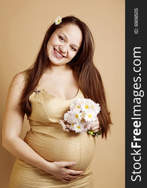 Happy pregnant woman with bouquet of flowers on beige studio background