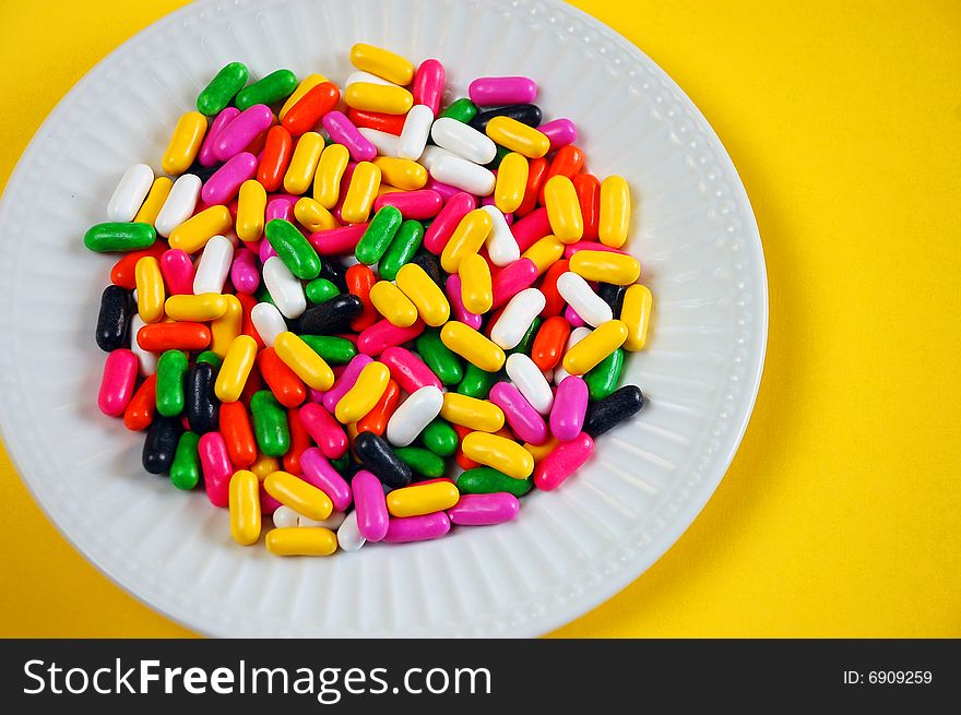 Colorful candy mix on white plate against yellow background