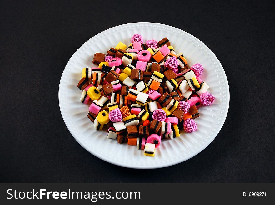 Colorful candy mix on white plate against black background