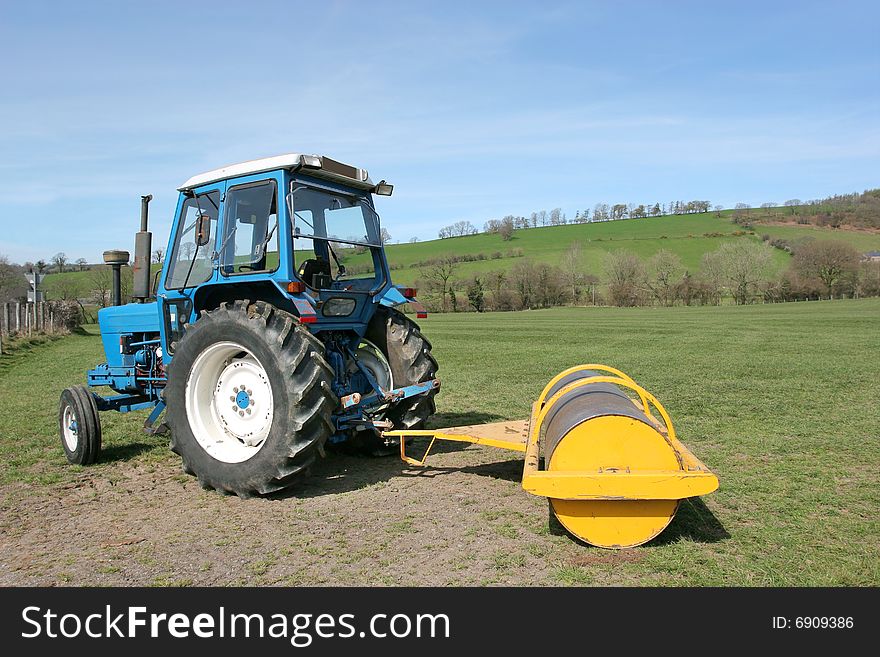 Tractor with yellow roller attached standing idle on farmland in rural countryside in spring. Farmers roll grass in spring to promote growth. Tractor with yellow roller attached standing idle on farmland in rural countryside in spring. Farmers roll grass in spring to promote growth.