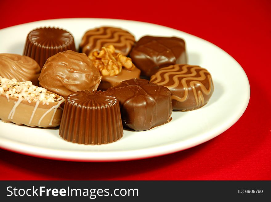 Assorted chocolates on white plate against red background