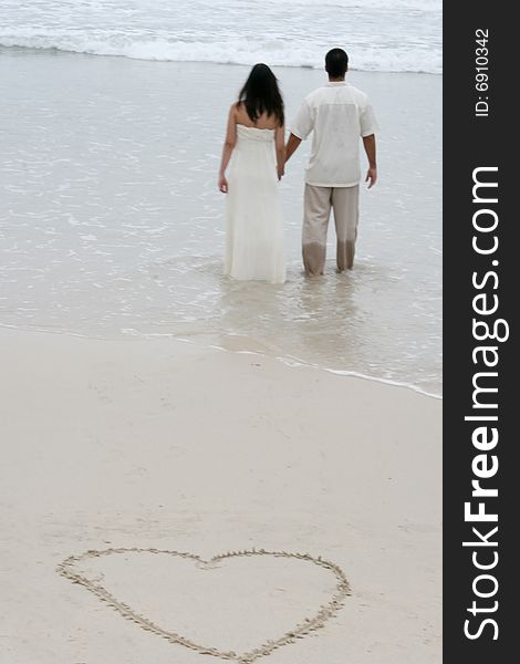 Heart in the sand with bride and groom walking towards the ocean. Heart in the sand with bride and groom walking towards the ocean.