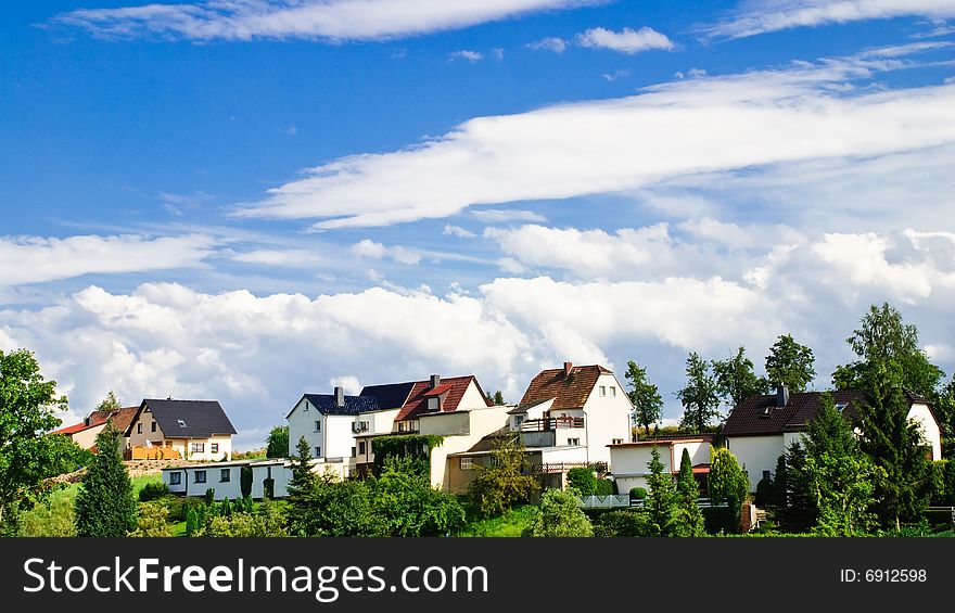 Village against the summer blue sky with white clouds on a green hill. Village against the summer blue sky with white clouds on a green hill