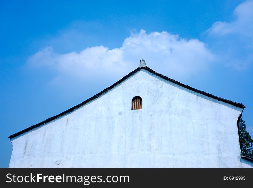 A white wall of a chinese traditional room with a little window under blue sky and white cloud. A white wall of a chinese traditional room with a little window under blue sky and white cloud.