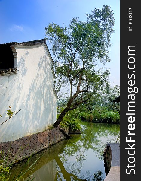 A chinese traditional village room by the river. there is a tree sticking in the white wall.