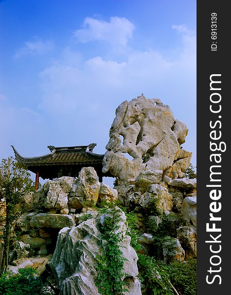 A chinese traditional gloriette on artistic stone hill under blue sky and white cloud. A chinese traditional gloriette on artistic stone hill under blue sky and white cloud.