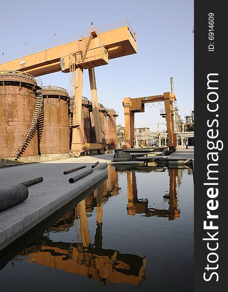 Crane and oil tanks in the factory with reflections. Crane and oil tanks in the factory with reflections