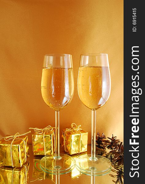 Two glasses with champagne and gift near on gold background