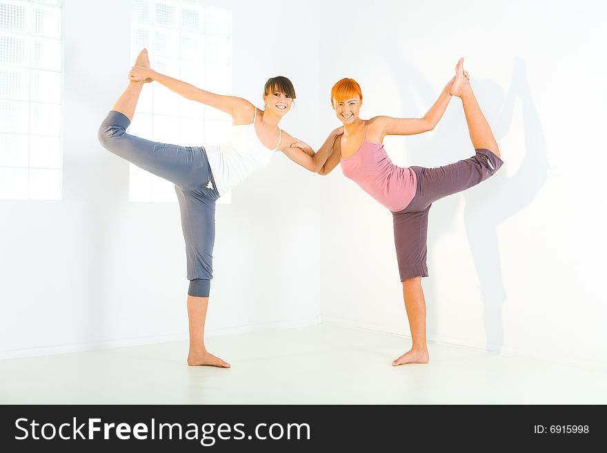 Two young women doing stretching exercises. They're looking at camera. Two young women doing stretching exercises. They're looking at camera.