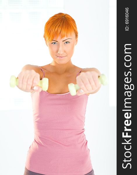 Young woman doing fitness exercise with dumbbells. She's looking at camera. Front view. Young woman doing fitness exercise with dumbbells. She's looking at camera. Front view.