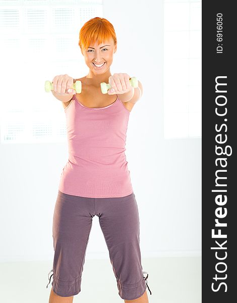 Young woman doing fitness exercise with dumbbells. She's looking at camera. Front view. Young woman doing fitness exercise with dumbbells. She's looking at camera. Front view.