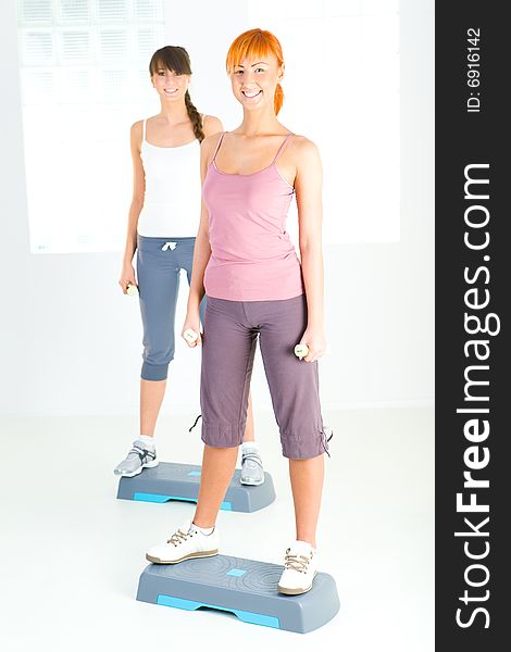 Two young women doing exercise on aerobic step. They're looking at camera. Front view. Two young women doing exercise on aerobic step. They're looking at camera. Front view.