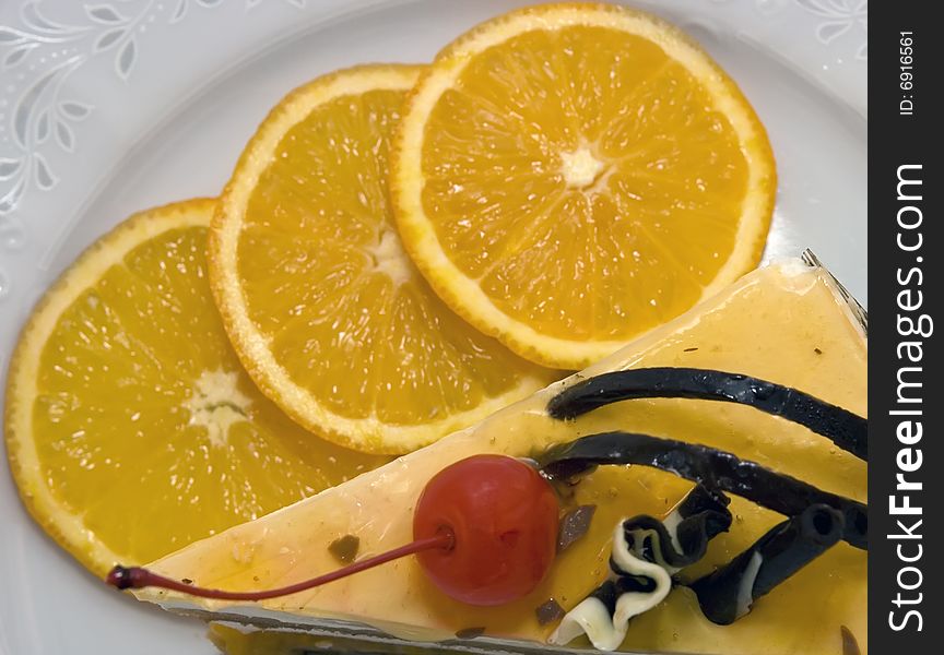 Piece of cake with cherry and three oranges on the dish