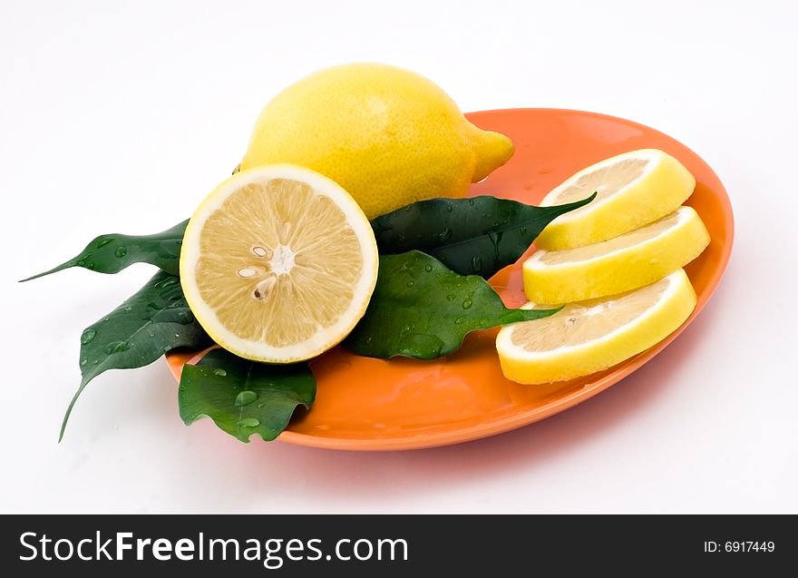 Lemon with green leaves on the orange plate. Lemon with green leaves on the orange plate