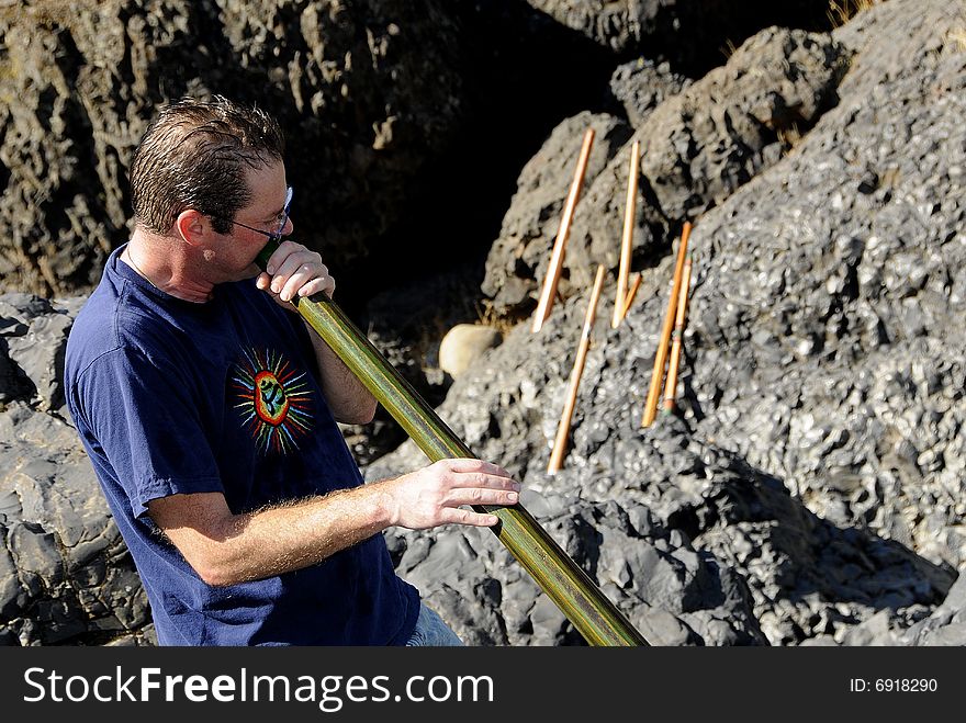 Custom Handcrafted Didgeridoo Master Playing in Canyon with Array of Didgeridoo's on Distant Rock Wall. Custom Handcrafted Didgeridoo Master Playing in Canyon with Array of Didgeridoo's on Distant Rock Wall