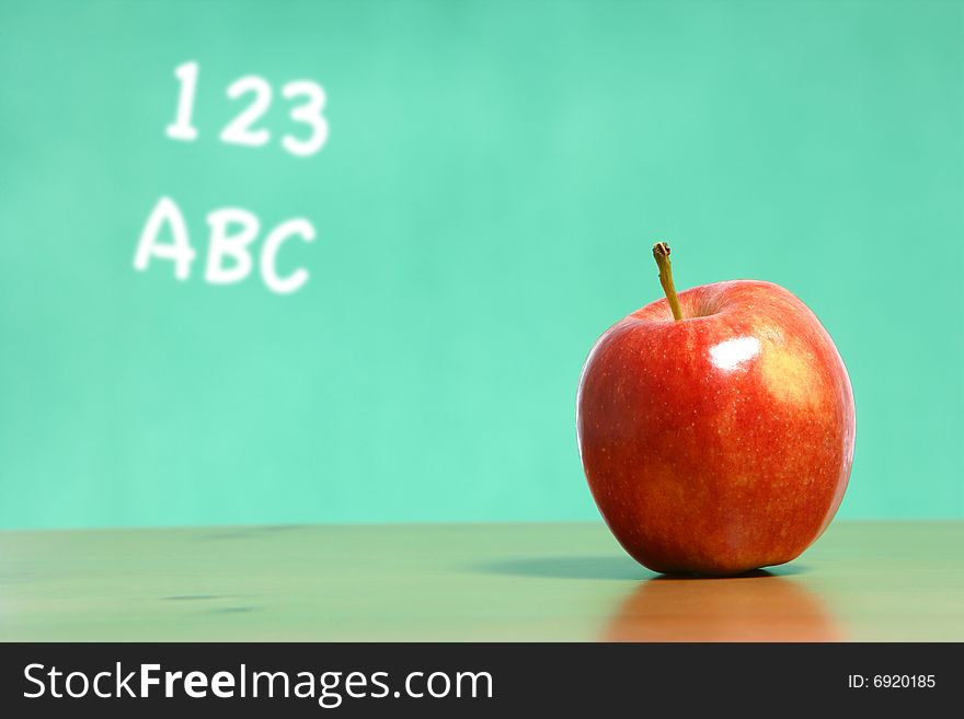 An apple on a desk in a classroom with 123 abc