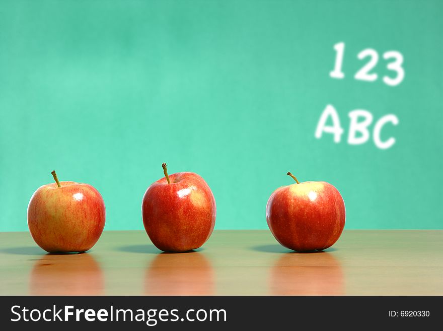 An apple on a desk in a classroom with 123 abc
