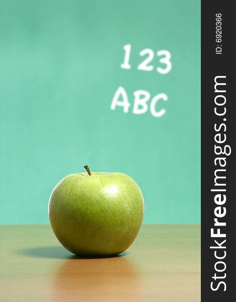 An apple on a desk in a classroom with 123 abc