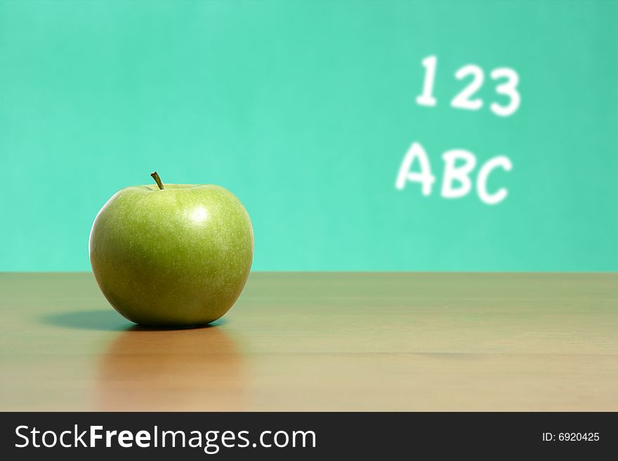 An apple on a desk in a classroom with 123 abc