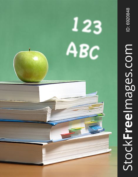 An apple on a stack of books on the teachers desk. An apple on a stack of books on the teachers desk