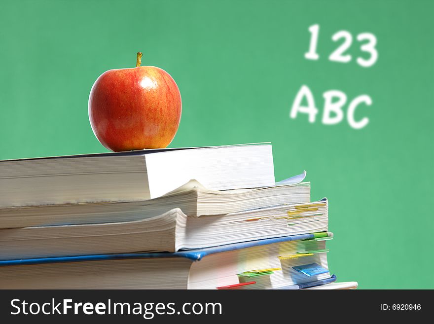 An apple on a stack of books on the teachers desk. An apple on a stack of books on the teachers desk