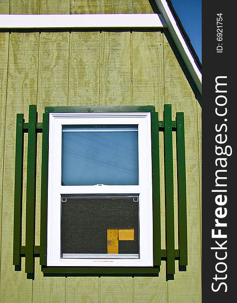 Barn window with green frame and green wall and blue sky