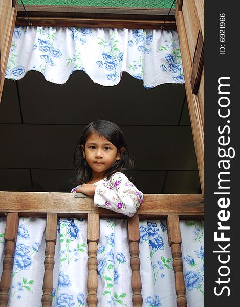 A Malaysian girl wearing malay traditional clothe standing by window in a traditional malay house.